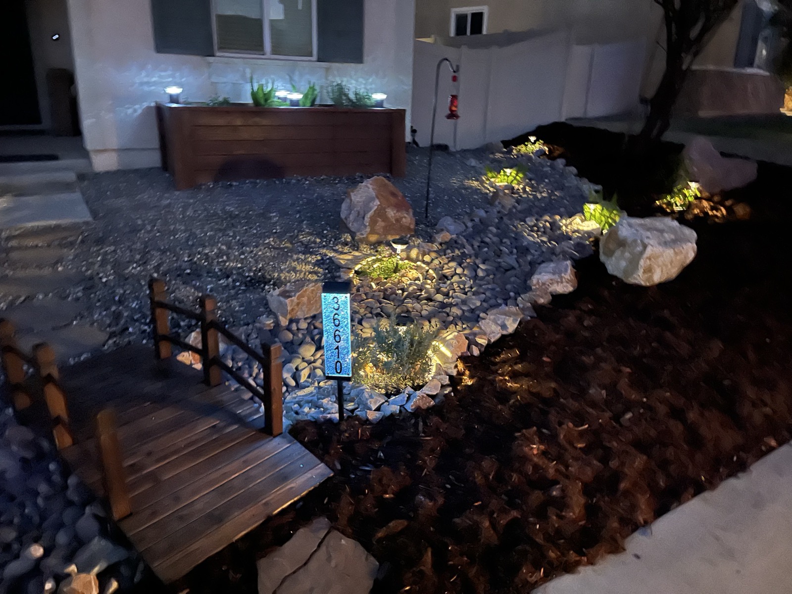 Nighttime landscape with decorative bridge, rock river, and pathway lighting in San Jacinto