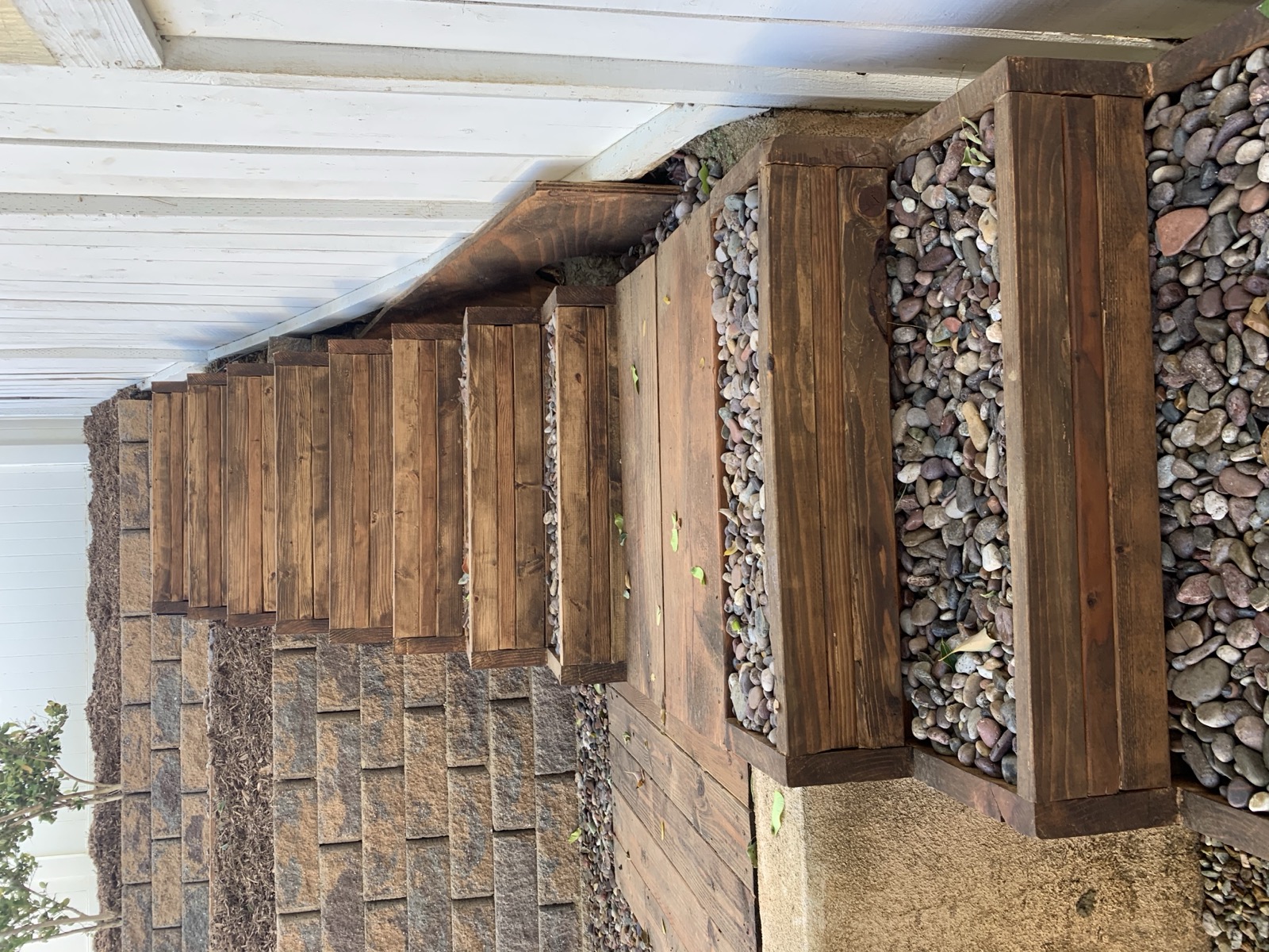 Custom stained wood planter boxes with river rock fill between pavers